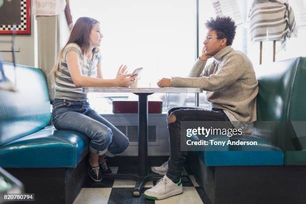 teenage girl and boy in booth at retro cafe with phone - boy and girl talking fotografías e imágenes de stock