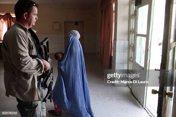 Woman in a burqa carries a child past an armed civilian contractor from the private company "Armored Group" in the city hospital during a Provincial...