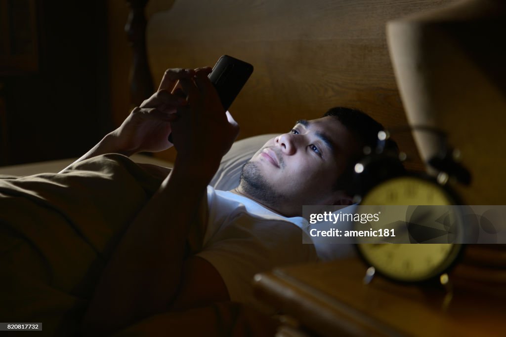 Young man using a smartphone in his bed at night