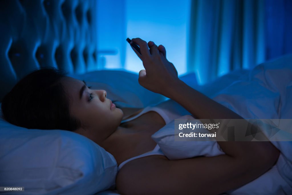 Asiatische Frauen nutzen das Smartphone auf dem Bett, bevor sie schlafen in der Nacht. Mobile-Süchtigen Konzept.