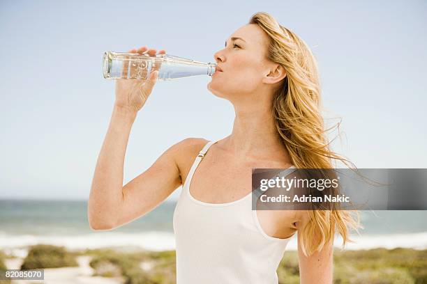 girl drinking from glass bottle at beach. - woman drinking water from bottle stock-fotos und bilder