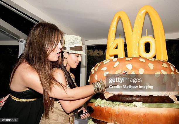 Khloe Kardashian and Kim Kardashian look at a giant 'Big Mac' burger-themed birthday cake during the McDonald's Big Mac 40th Birthday Party at...