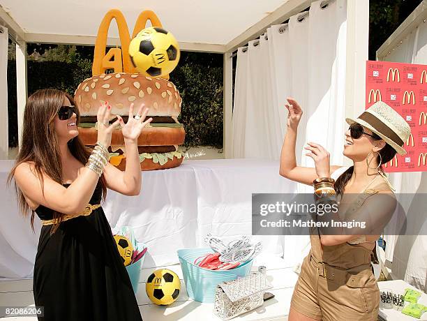 Khloe Kardashian and Kim Kardashian play catch with a football near a giant burger during the McDonald's Big Mac 40th Birthday Party at Project Beach...