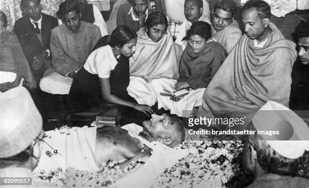 Indian statesman Mohandas Karamchand Gandhi lies in state at Birla House after his assassination, as one of his grandnieces places flower petals on...