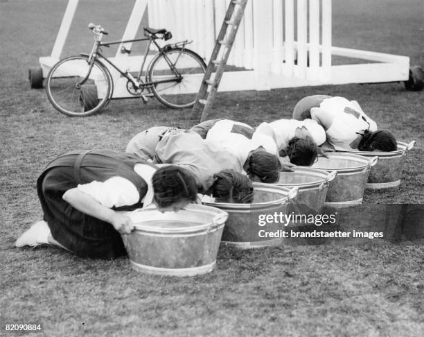 Women trying to fish lemons out of a bowl of water, England, Photograph, March 23rd 1933 [Frauen beim Versuch eine Zitrone aus dem Wasser zu fischen,...