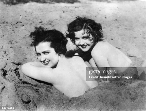 The actresses Nancy Carrol and Doris Hill lying at the beach burried in sand, America, Photogarphy, Around 1930 [Die Schauspielerinnen Nancy Carroll...