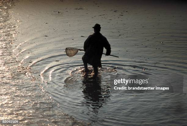 Silhouette of a fisherman standing in the water and holding a fishing net in his hands, Austria, Around 2004 [Silhouette eines im Wasser stehenden...