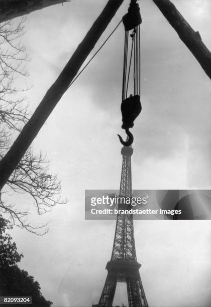 The picture shows th eiffel tower in Paris, In the foreground a construction crane, Due to the angle, the photographer has chosen, it looks like the...