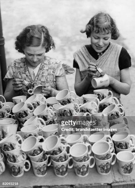 Two girls finishing mugs with the portrait of Edard VIII, on the occasion of his coronation, Photograph, England, May 13th 1936 [Zwei Arbeiterinnen...