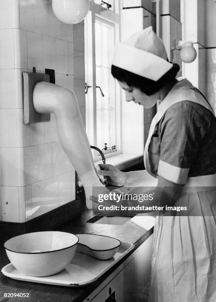 Nurse learning how to bandage on a plastic leg, London, Photograph, Around 1930 [Krankenschwester lernt das Anlegen einer Bandage bei einem...