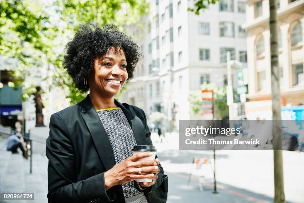 smiling businesswoman standing on city sidewalk with cup of coffee - mature women cafe stock pictures, royalty-free photos & images