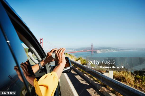 Woman taking photo of Golden Gate Bridge out of car window with smartphone