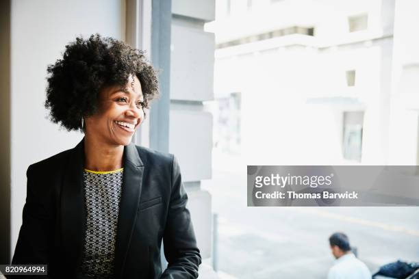 smiling businesswoman sitting in coffee shop looking out window - casaco preto - fotografias e filmes do acervo