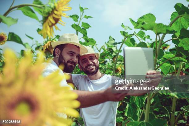 deux paysans souriants rendant selfie avec digital tablette en champ de tournesols - agriculteur selfie photos et images de collection