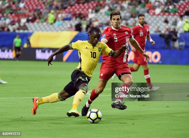 Darren Mattocks of Jamaica brings the ball up field while being defended by Dejan Jakovic of Canada in a quarterfinal match during the CONCACAF Gold...