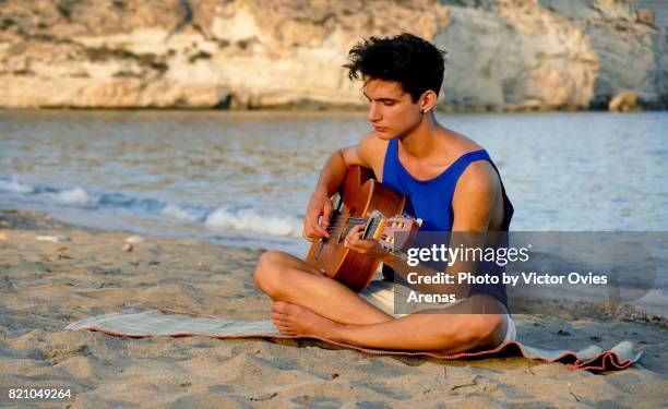 teen male model playing spanish guitar on the beach - teen boy shorts imagens e fotografias de stock