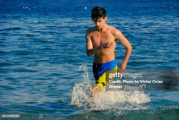 shirtless teen male model running in the water on the sea shore - teen boy shorts stockfoto's en -beelden