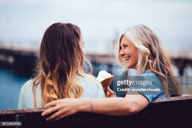 reife oma und enkelin essen eis sitzen auf einer bank - teenagers eating with mum stock-fotos und bilder