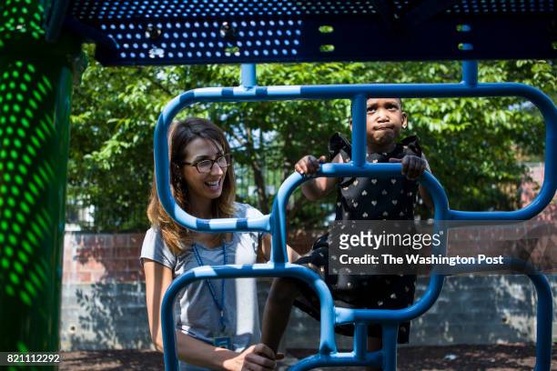 Physical therapist Lauren Fery spots her student Kamille Davis as she climbs up the playground ladder at St. Coletta school on July 19, 2017 in...