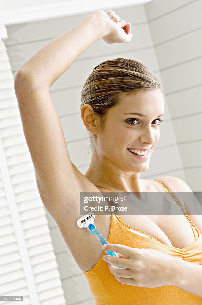 Reflection of a young woman shaving her armpit hair