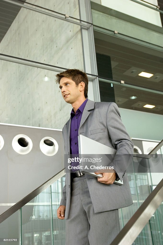 Businessman holding a laptop and walking down a staircase