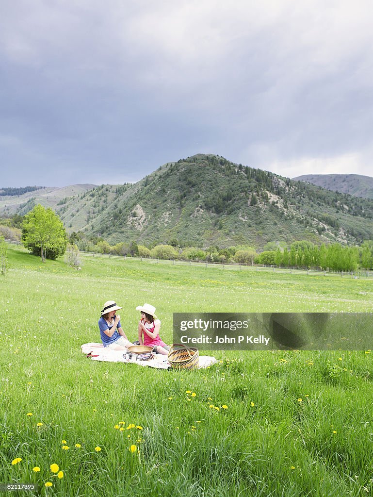 Two pre-teen girls having a picnic in a grassy field.