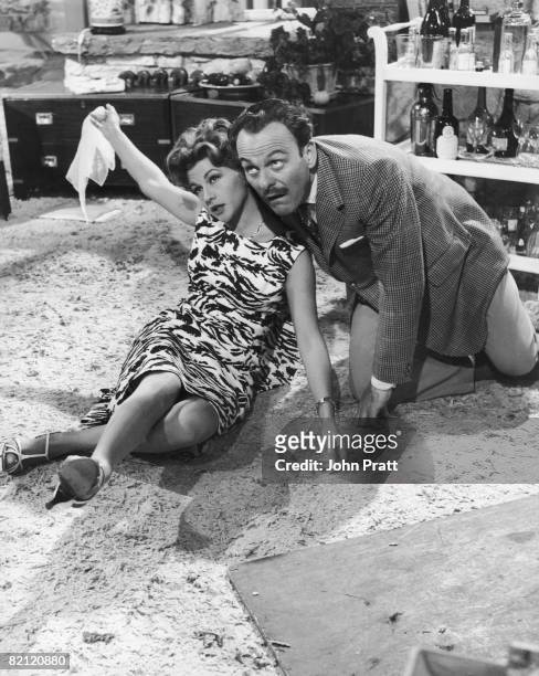 English comic actor Terry-Thomas rolls around on the rug with French actress Nicole Maurey whilst filming a scene for his latest film 'His and Hers',...
