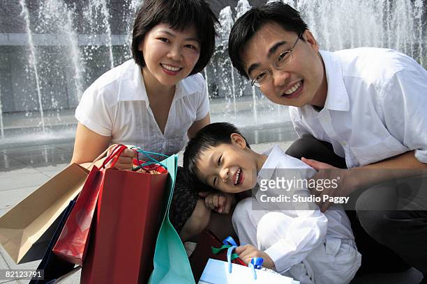 portrait of a mid adult couple smiling with their son in a park and smiling - singapore shopping family stock pictures, royalty-free photos & images