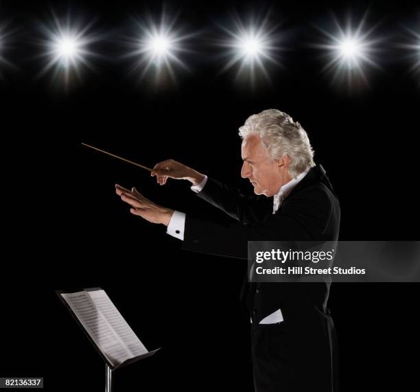 man in tuxedo conducting under lights - notenständer stock-fotos und bilder