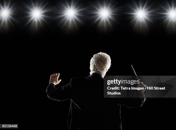 man in tuxedo conducting under lights - orchestra conductor foto e immagini stock