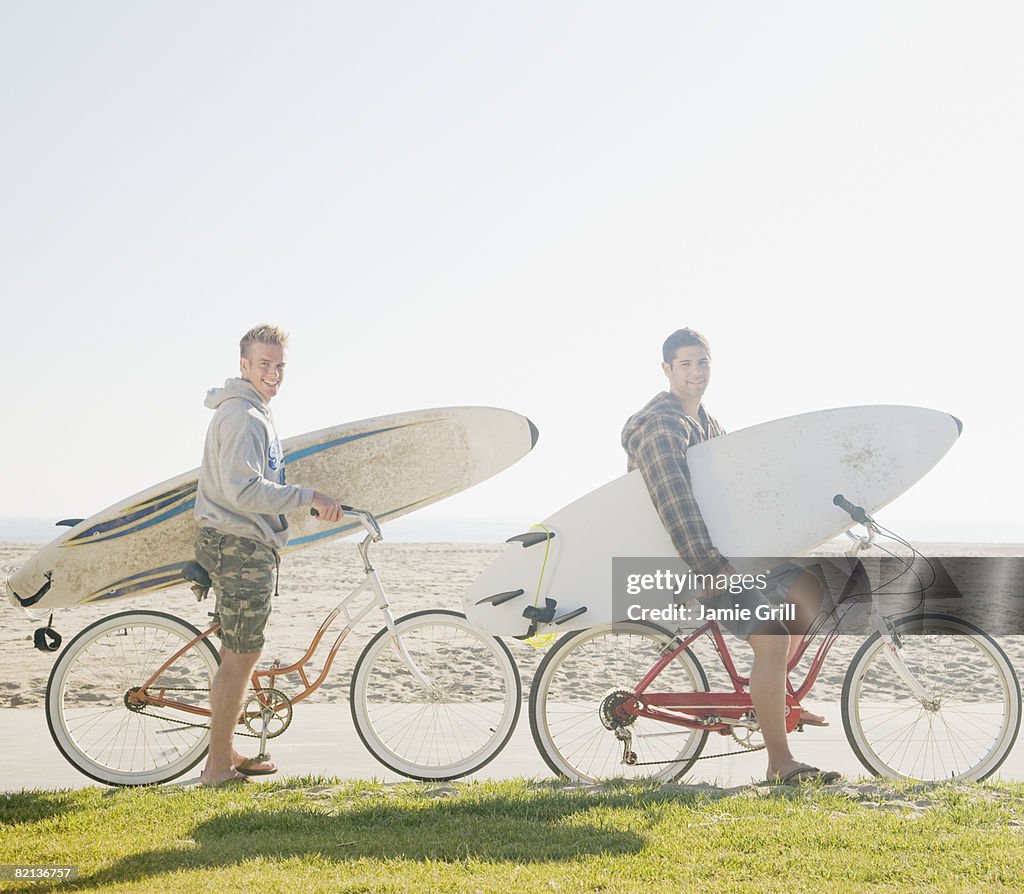 Two men with surfboards on bicycles