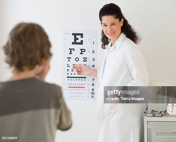 hispanic female doctor pointing at eye chart for child - ophthalmologist chart stock pictures, royalty-free photos & images