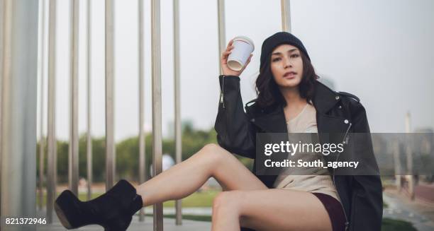 portrait of a hipster woman sitting outdoors and holding coffee - leather shorts stock pictures, royalty-free photos & images