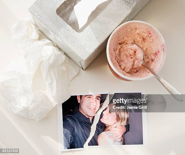 ripped photograph next to ice cream and tissues - relationship difficulties photos stock pictures, royalty-free photos & images
