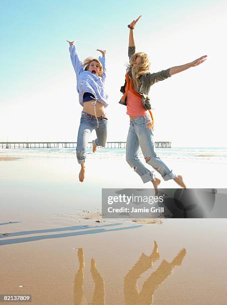 two women jumping on beach - venice california photos et images de collection