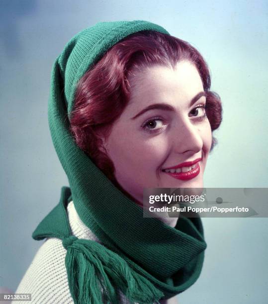 Circa 1950's, A portrait of an auburn haired girl wearing a green woollen hat and a white polo necked sweater with a green winter scarf wrapped...