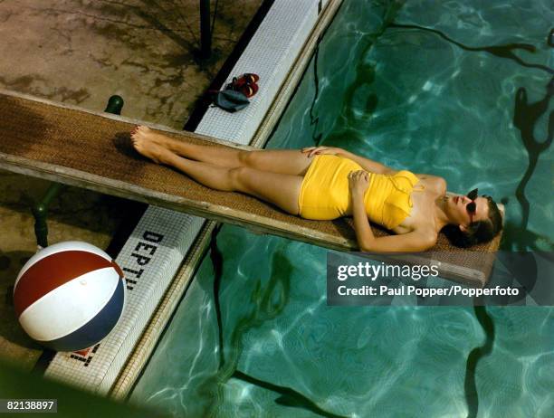 Fashion Swimwear, pic: circa 1950's, Woman wearing yellow swimsuit relaxing at the poolside