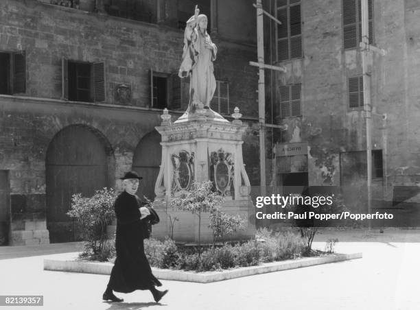 Travel, Religion, pic: circa 1960, Majorca, Palma, A religous man walks by a statue at The Bishop's Palace, Palma