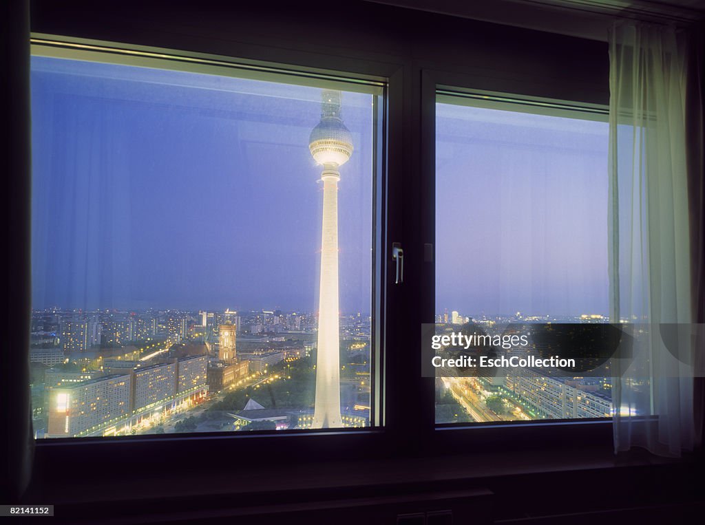 Window view of Alexander Platz at dusk with the Fernsehturm in front.