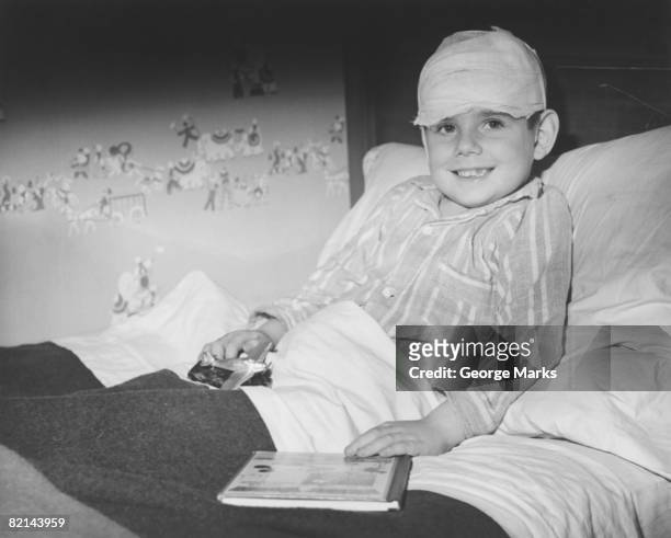 boy (8-9) with bandage on head sitting in bed, (b&w), portrait - head bandage stock-fotos und bilder