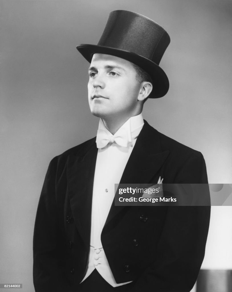 Man wearing tuxedo and top hat posing in studio, (B&W)