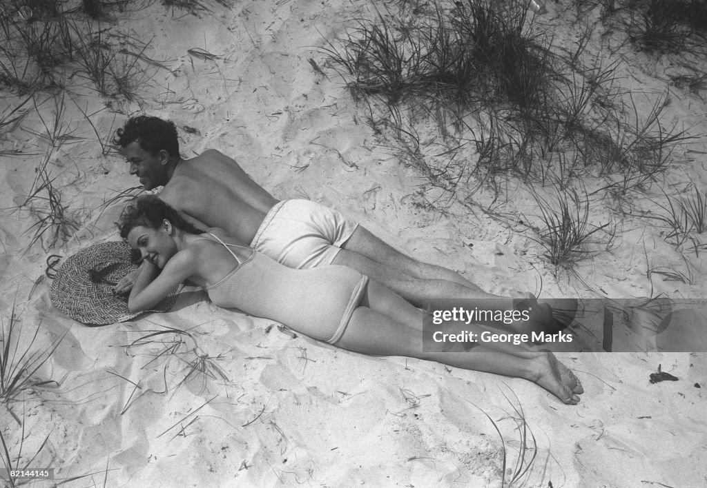 Couple relaxing on beach, (B&W), elevated view