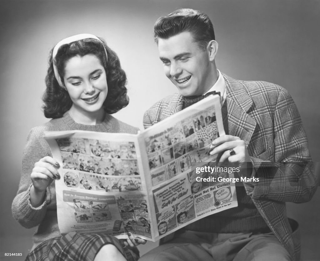 Young couple holding newspaper in studio, (B&W)
