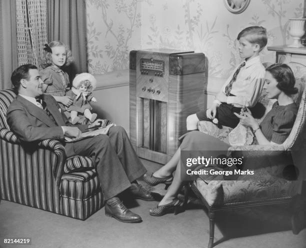family with two children (6-7, 8-9) sitting in living room, (b&w) - radio stockfoto's en -beelden