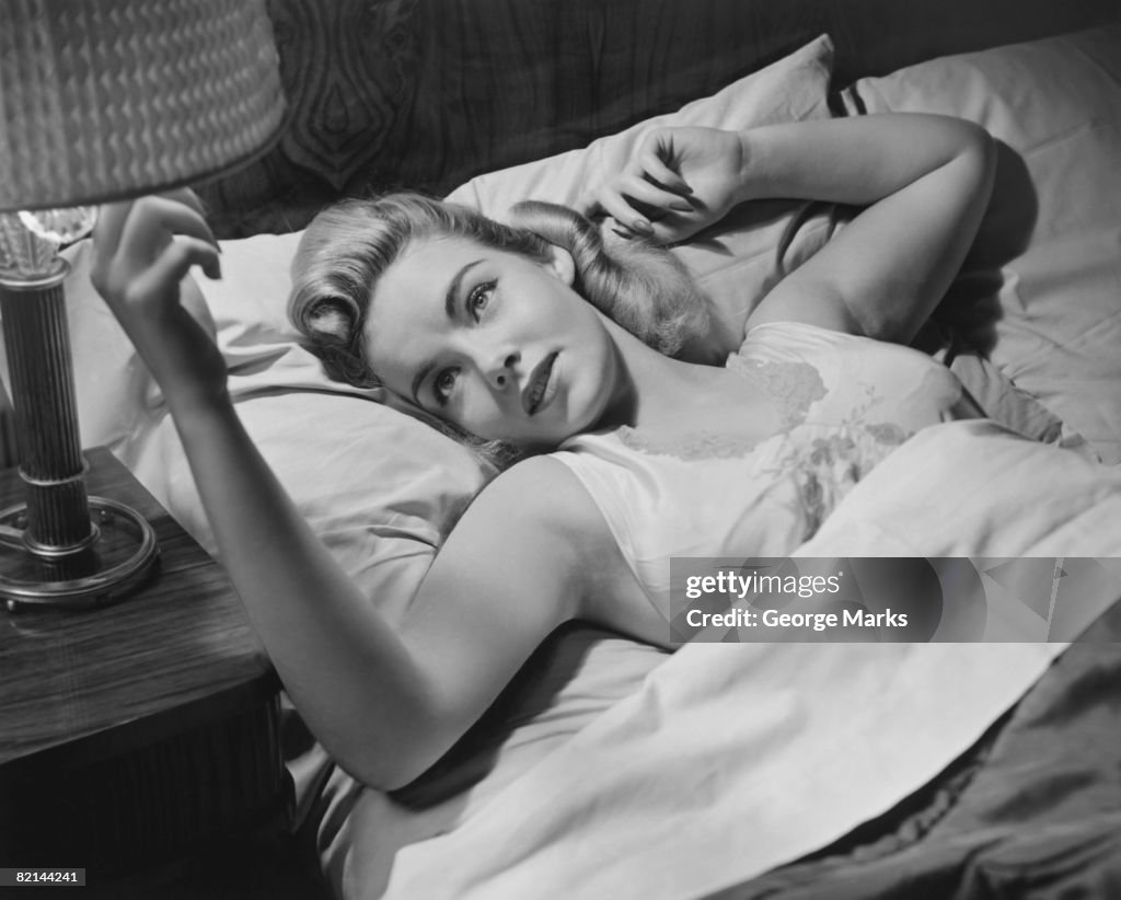 Woman lying on bed turning off lamp, (B&W),