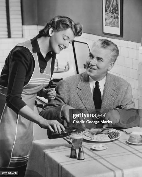 woman pouring beer from bottle for man eating dinner, (b&w) - gender stereotypes stock pictures, royalty-free photos & images