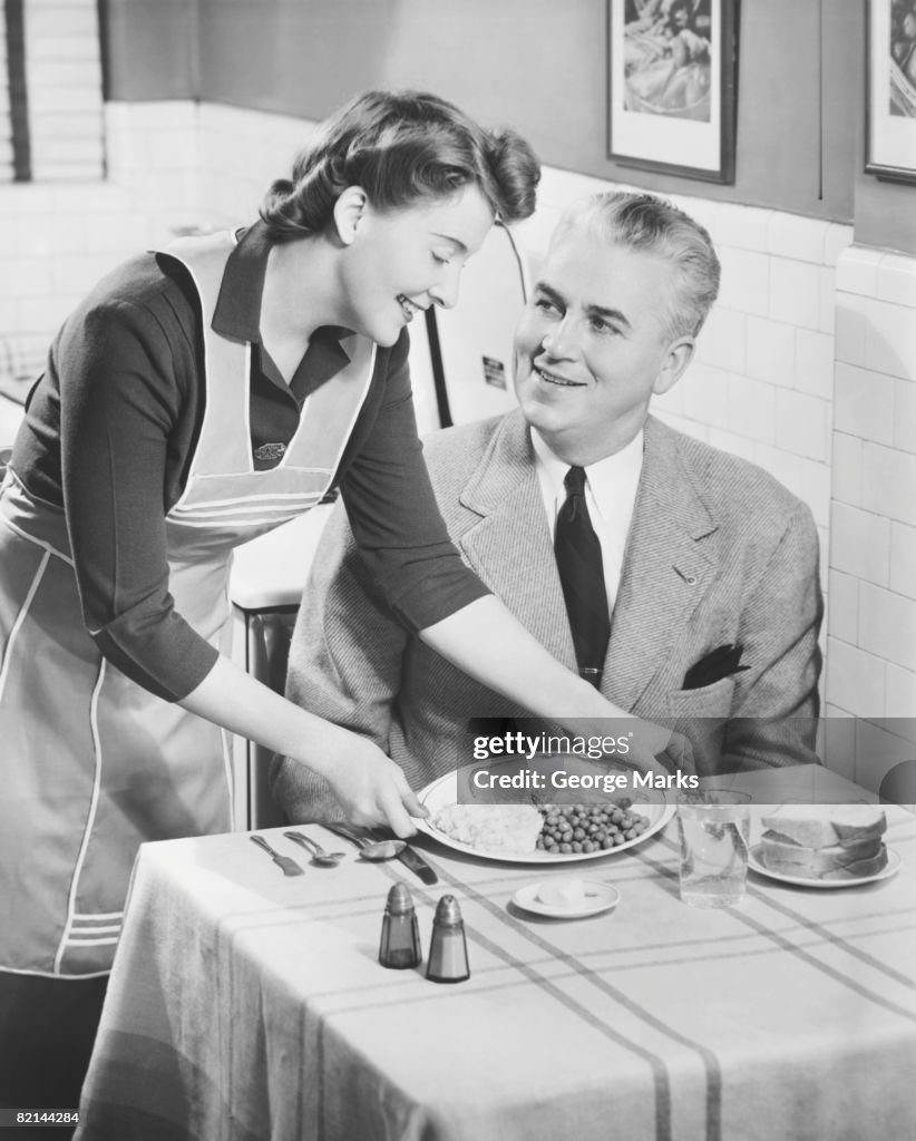 Woman serving dinner to husband, (B&W)