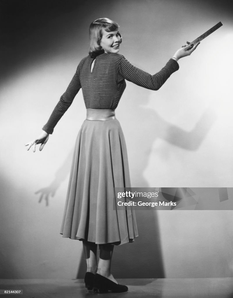 Woman pointing with ruler in studio, (B&W)