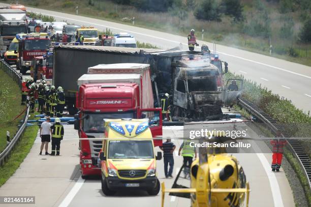 Firemen and emergency rescue crews stand near a truck that caught fire following an accident on the A13 highway heading north on July 24, 2017 near...