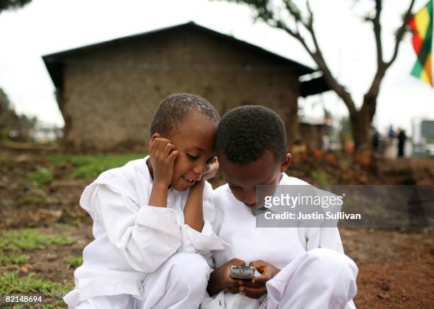 Two boys play with a cellular phone as former U.S. President Bill Clinton tours the Godino Health Center August 1, 2008 in Debre Zeit, Ethiopia....